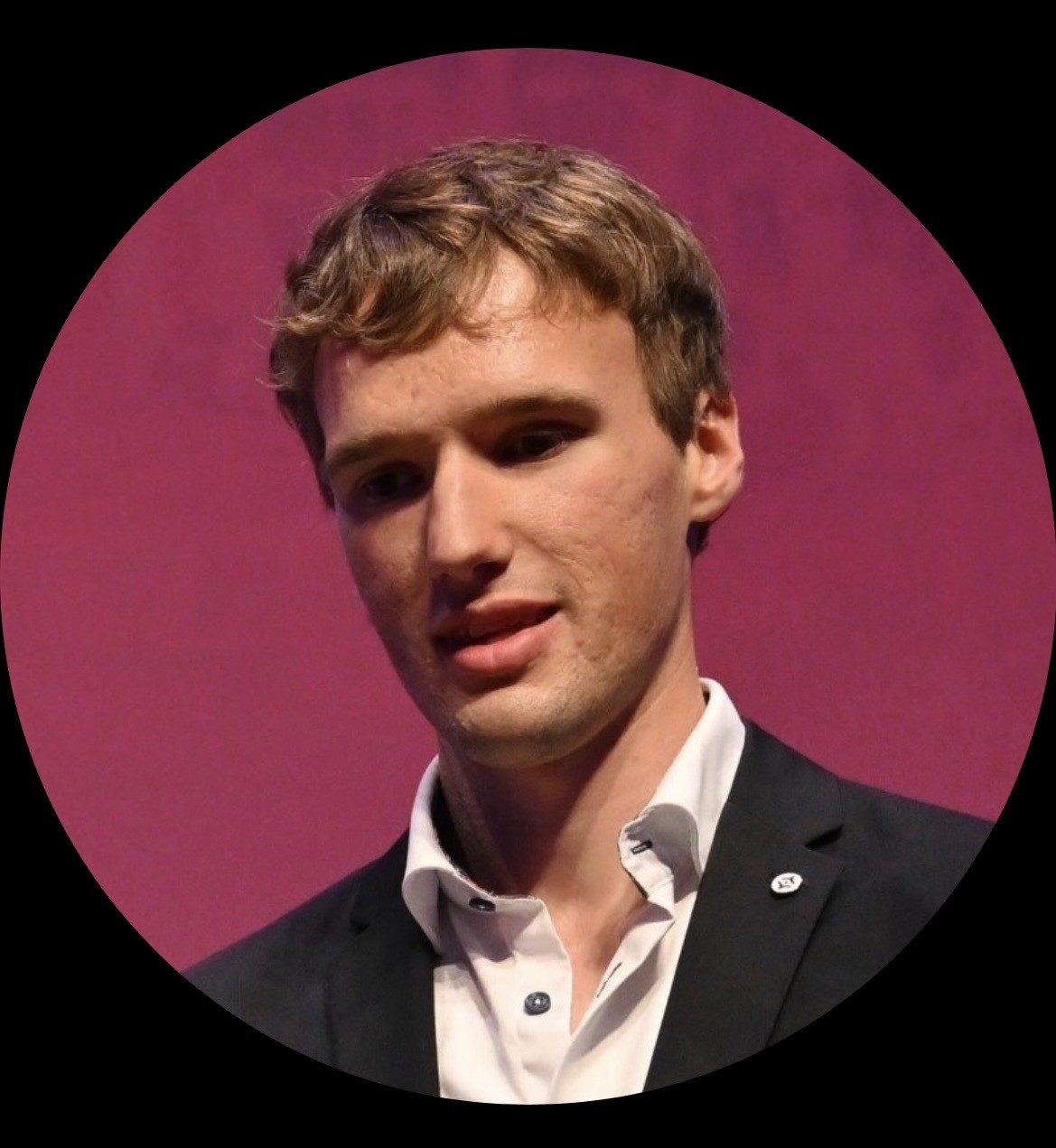 Portetfoto van een glimlachende Jesse Wienholts, tegen een paars-roze achtergrond in een zwart rond kader