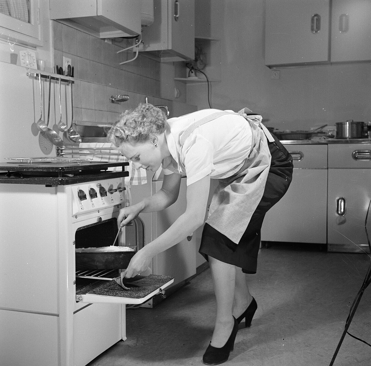 Zwart-wit foto van een huisvrouw in de jaren vijftig die voorover buigt om een taart uit de oven te halen