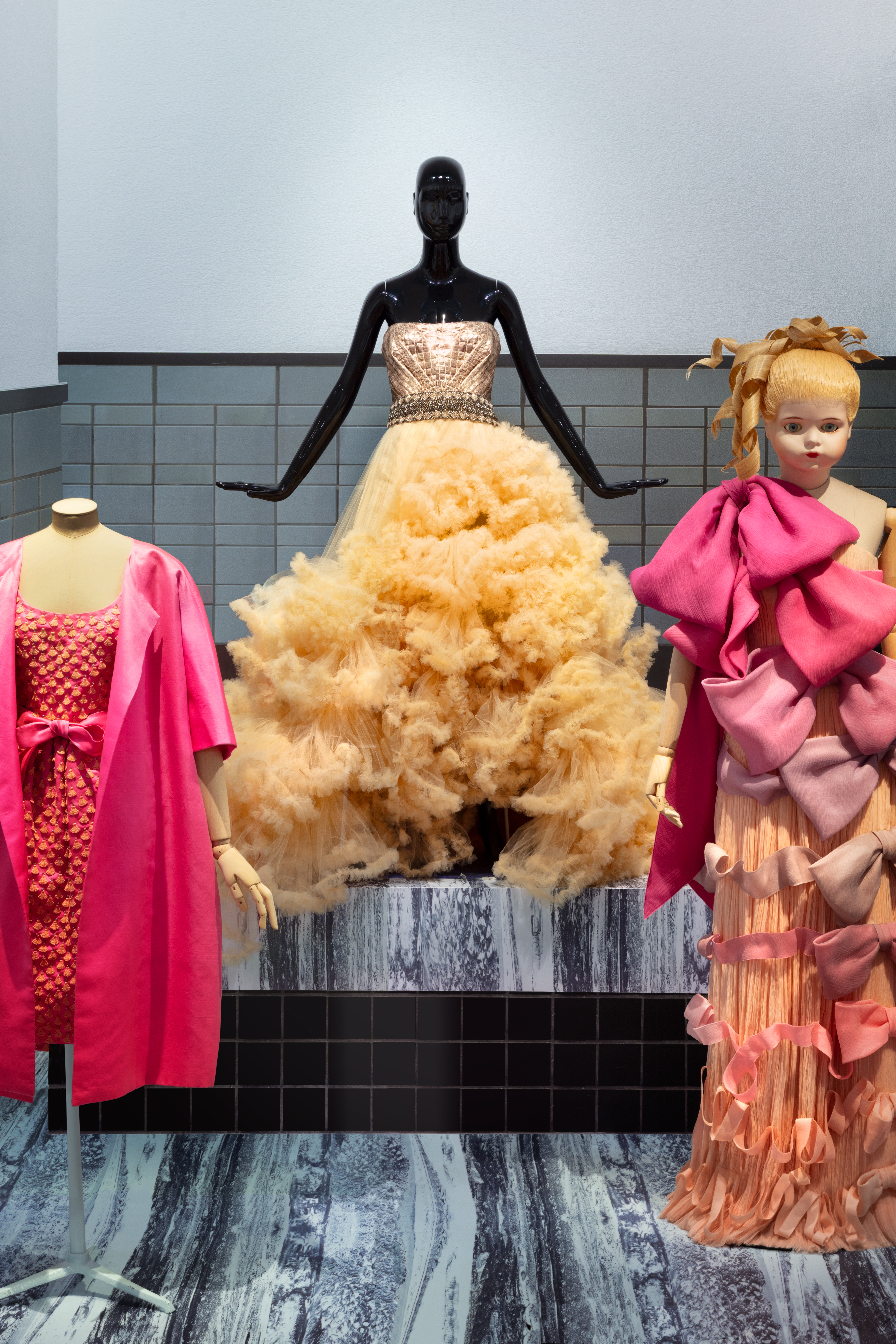 Drie sierlijke jurken op poppen in een tentoonstellingsruimte.