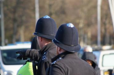 Twee Engelse politieagenten, op de rug gezien, wijzend. Op de achtergrond auto's.