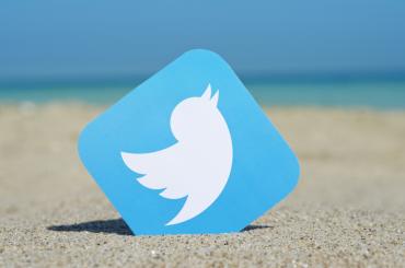 Twitterlogo in het zandgestoken, vage zee en horizon op de achtergrond