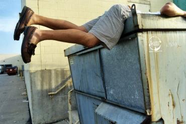 iemand hangt voorover over de rand van een vuilcontainer, je ziet alleen de benen naar buiten steken