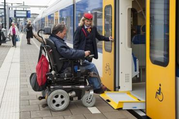 Man in rolstoel wordt door een conductrice de trein in geholpen met een rolstoelbrug
