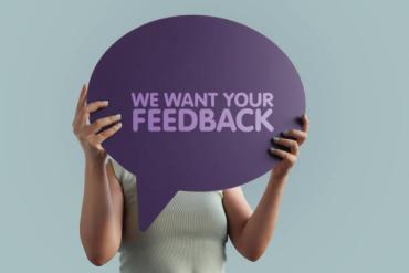 Vrouw houdt een tekstballon voor haar gezicht met daarop de tekst 'We want your feedback'