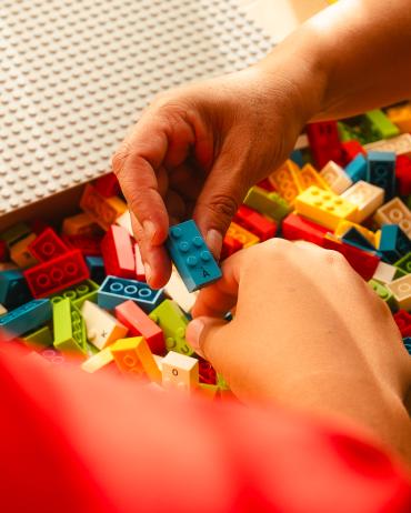 Iemand neemt een Braille Bricks Blokje met de letter 'A accent grave'uit een doos