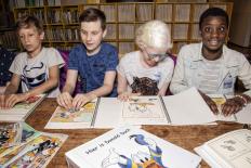 Vier kinderen achter een tafel die de Donald Duck in braille lezen 