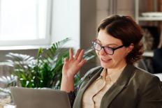 Vrouw met bril achter de laptop, zwaaiend naar het scherm